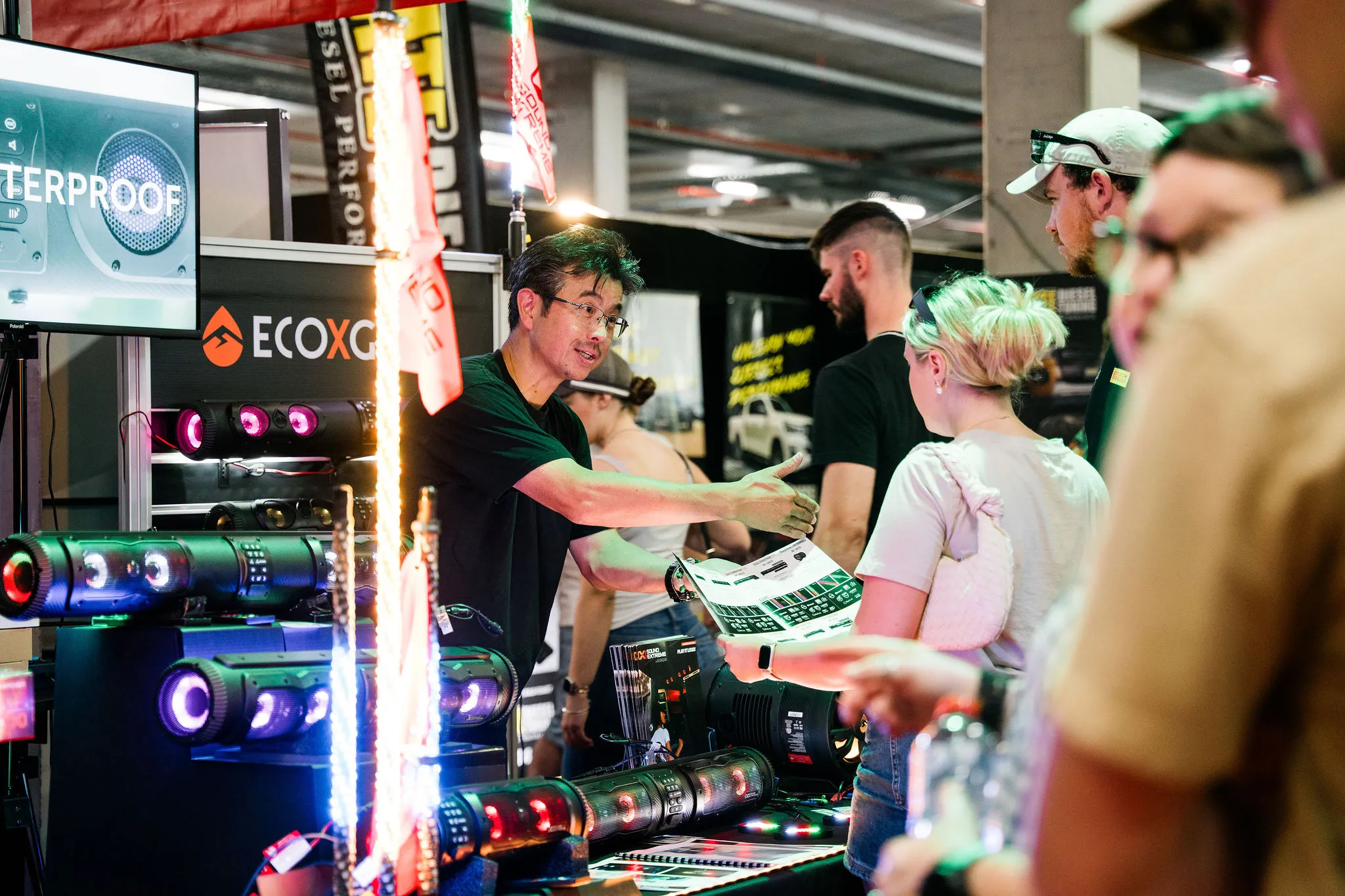 Exhibitor showing visitors an ECOXGEAR speaker brochure on a stand at the National 4x4 Outdoors Show Brisbane 2025